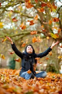 Autumn woman at the park throwing leaves in the air